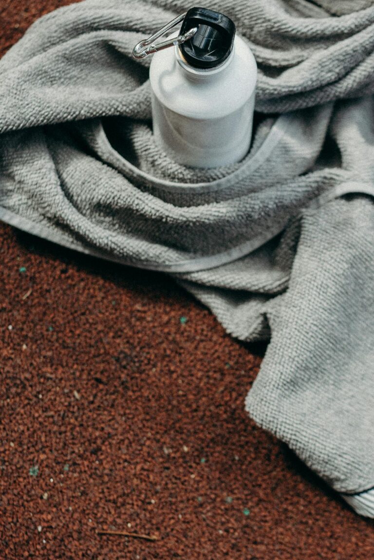 Stainless steel water bottle on a towel at a sports field, promoting sustainability.