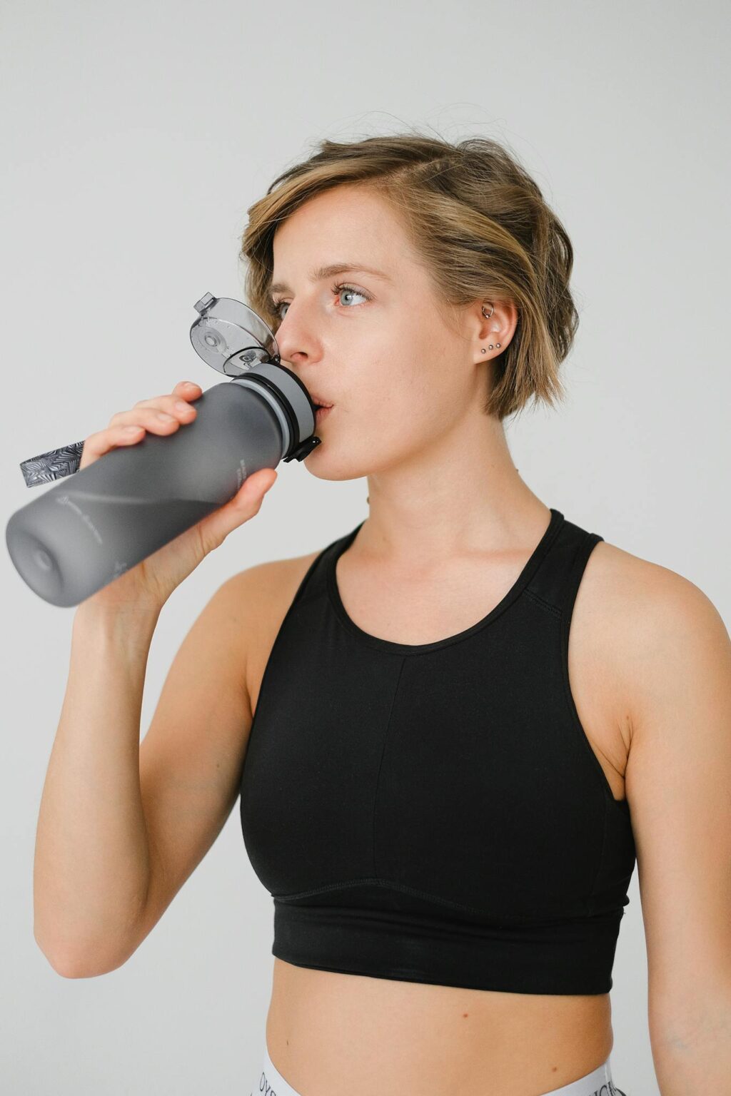 Young woman in athletic wear sipping water from a reusable bottle, promoting hydration and fitness.